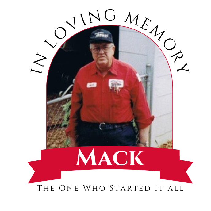 Man in red work shirt and black cap standing outdoors, with a red banner below reading “MACK”