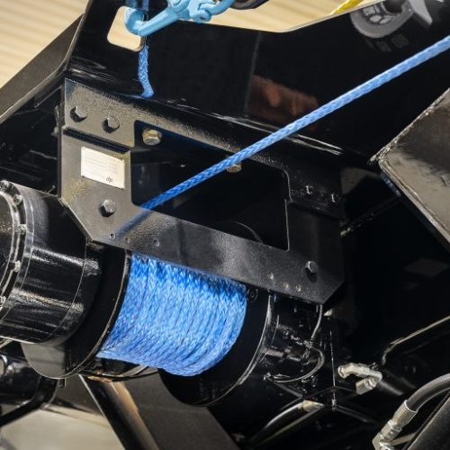 Close-up of black vehicle winch with blue synthetic rope wound on drum under chassis mount