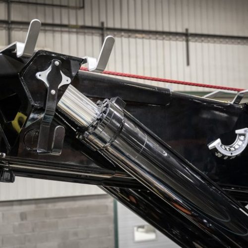 Close-up of a black industrial boom with a hydraulic cylinder, metal brackets, and yellow lifting ring in a workshop