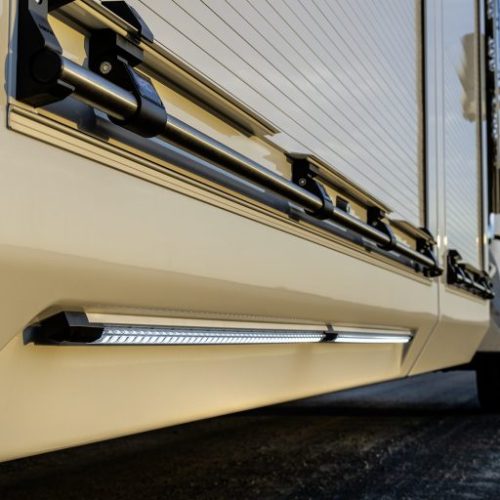 LED underbody light bar mounted beneath a truck or trailer side panel, illuminating the road surface at dusk