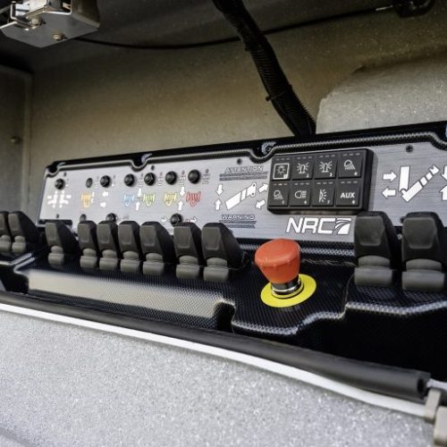 Vehicle control panel with toggle switches, labeled buttons, and a red emergency stop button in a compartment