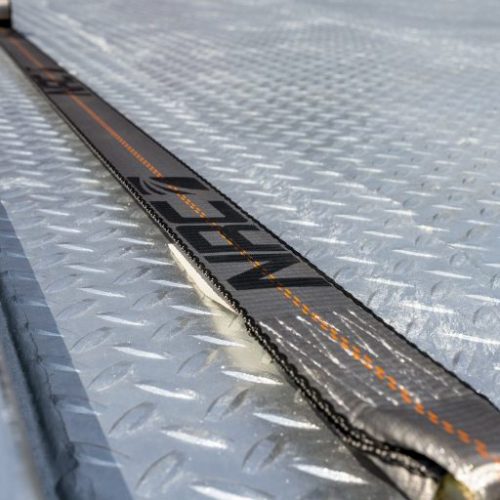 Close-up of a black webbing strap with orange stitching on a diamond-plate metal surface
