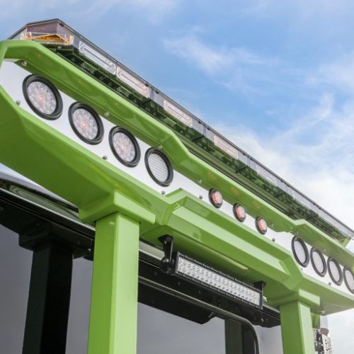 Low-angle close-up of green industrial platform with circular work lights and LED light bar against a blue sky