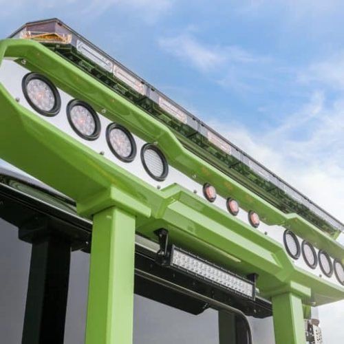 Low-angle close-up of green industrial platform with circular work lights and LED light bar against a blue sky