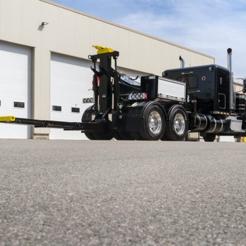 Black semi truck with extended quick-swap dolly frame parked outside industrial garage doors